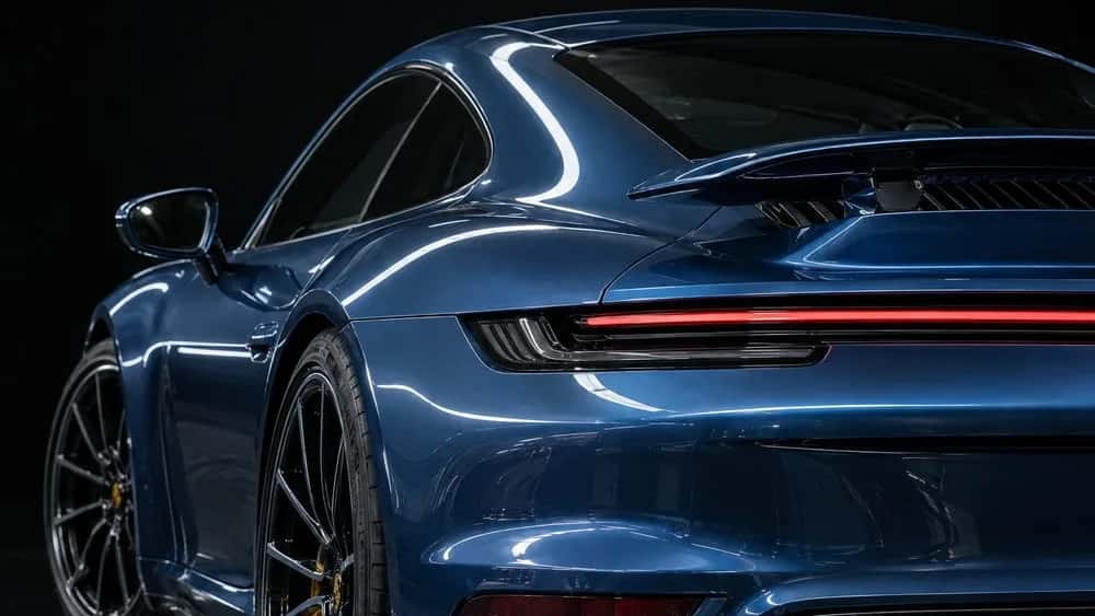 A deep blue Porsche 911 Turbo S across a wide frame, one sharp unbroken highlight running from the roofline along the shoulder to the tail.