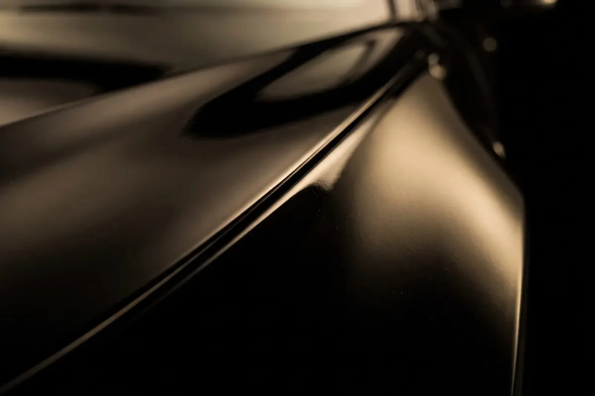 Close-up of a dark painted body edge where two panels meet, a soft warm-toned highlight running the length of the crease.